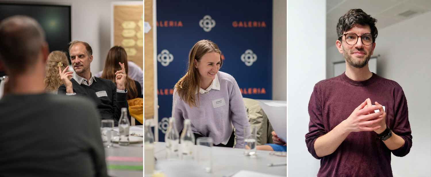 Drei Personen in einem Workshopraum während einer Diskussion und Gruppenarbeit. Links ein Mann im Gespräch, in der Mitte eine Frau, die lächelnd an einem Tisch sitzt, rechts ein Mann, der vor der Gruppe spricht.
